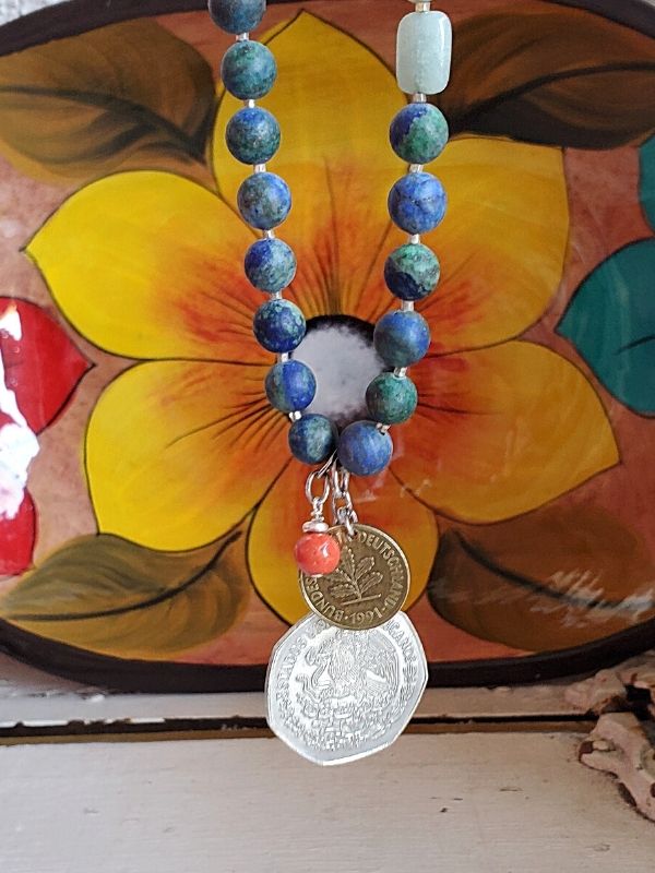 blue gemstone necklace hangs in front of colorful folkart
